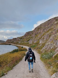 person in black jacket and blue denim jeans walking on pathway near body of water during