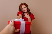 a woman holding a red gift box with a white ribbon