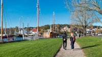 Couple walking on path by harbor with sailboats