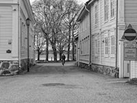Person cycling between wooden buildings towards a lake.