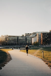 Person running on park path with city buildings at sunset.