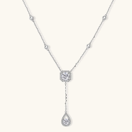 Sterling silver necklace with cushion-cut moissanite in halo setting and teardrop pendant, displayed on cream background.